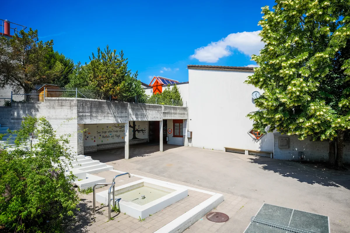 Schulhausfassade mit Uhr und Eingangsbereich.